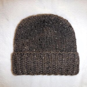 May include: A brown knitted beanie hat with a folded-up brim. The hat is made from a textured yarn with white flecks. A warm winter accessory.