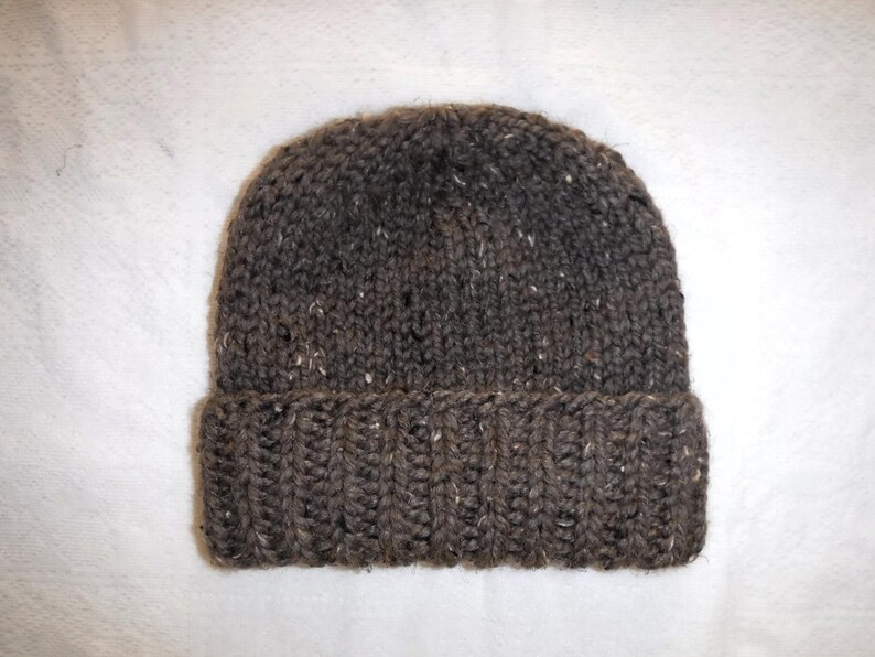 May include: A brown knitted beanie hat with a folded-up brim. The hat is made from a textured yarn with white flecks. A warm winter accessory.