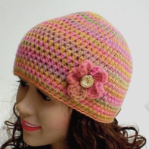 May include: A pink, green, and orange crocheted hat with a pink crocheted flower and a gold button.
