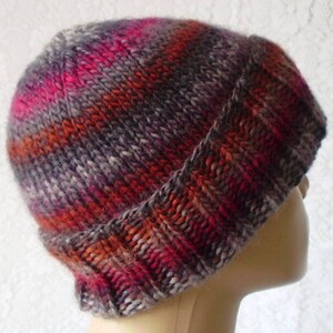 May include: A knitted beanie hat with a striped pattern in shades of grey, pink, orange, and red.