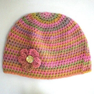 May include: A crocheted hat in shades of pink, green, and brown with a flower embellishment. The flower has a gold button in the center.