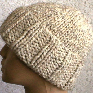 May include: A beige knitted hat with a textured pattern. The hat is made from thick yarn and has a slouchy fit.