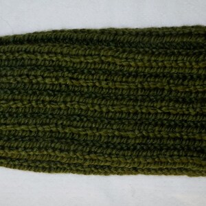 Op de afbeelding: Een olijfgroene gebreide beanie. De hoed is gemaakt van een dik, geribbeld gebreid materiaal. De hoed is effen van kleur en heeft een eenvoudig, klassiek ontwerp. Deze warme hoed is perfect voor koud weer.