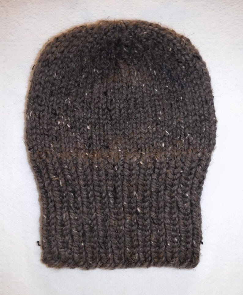 May include: A dark brown knitted beanie hat with a ribbed brim. The hat is made of a thick yarn with white flecks. The top of the hat has a tighter knit, creating a snug fit.