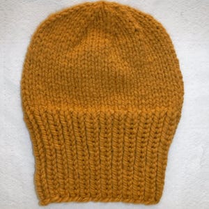 May include: Mustard yellow knit beanie hat. The hat is made of thick yarn and features a ribbed brim. The top of the hat has a close knit pattern. This warm hat is perfect for cold weather.