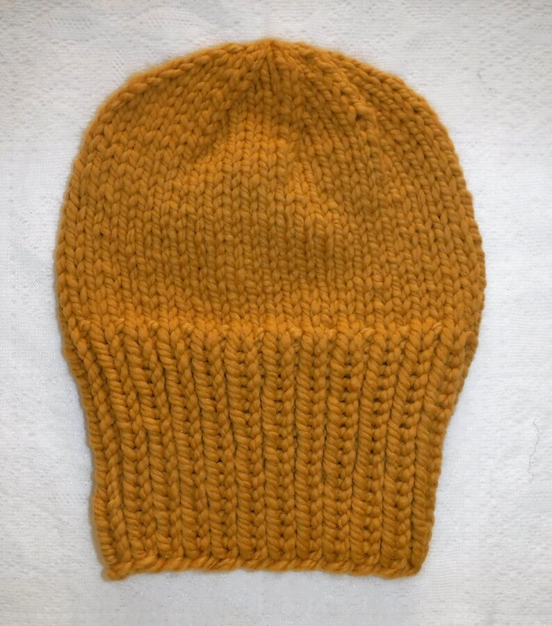 May include: Mustard yellow knit beanie hat. The hat is made of thick yarn and features a ribbed brim. The top of the hat has a close knit pattern. This warm hat is perfect for cold weather.