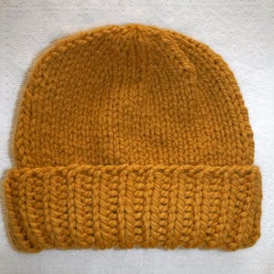 May include: Mustard yellow knit beanie hat. The hat features a ribbed brim and a chunky knit design. The hat is made of a soft, warm material, perfect for cold weather. The hat is a solid color and has a classic style.