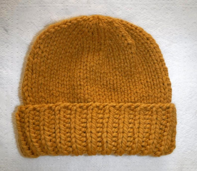 May include: Mustard yellow knit beanie hat. The hat features a ribbed brim and a chunky knit design. The hat is made of a soft, warm material, perfect for cold weather. The hat is a solid color and has a classic style.