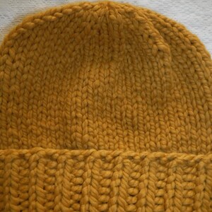 May include: Mustard yellow knit beanie hat. The hat is made of thick, chunky yarn with a ribbed brim and a close knit crown. The color is a warm, earthy tone, perfect for cold weather. The hat is a simple, classic design.