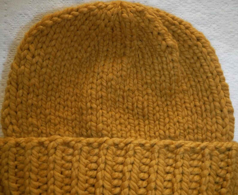 May include: Mustard yellow knit beanie hat. The hat is made of thick, chunky yarn with a ribbed brim and a close knit crown. The color is a warm, earthy tone, perfect for cold weather. The hat is a simple, classic design.
