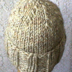 May include: A beige knitted hat with a ribbed brim. The hat is made from a soft, textured yarn.