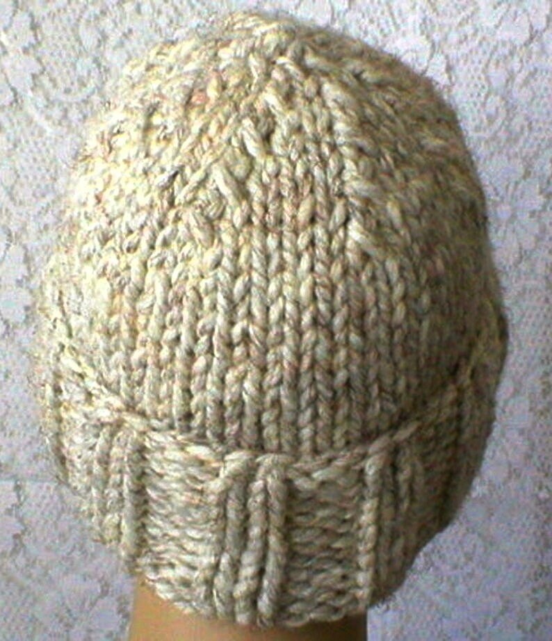 May include: A beige knitted hat with a ribbed brim. The hat is made from a soft, textured yarn.