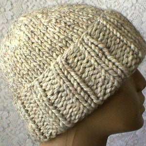 May include: A beige knitted hat with a textured pattern. The hat is made from thick yarn and has a slouchy fit.