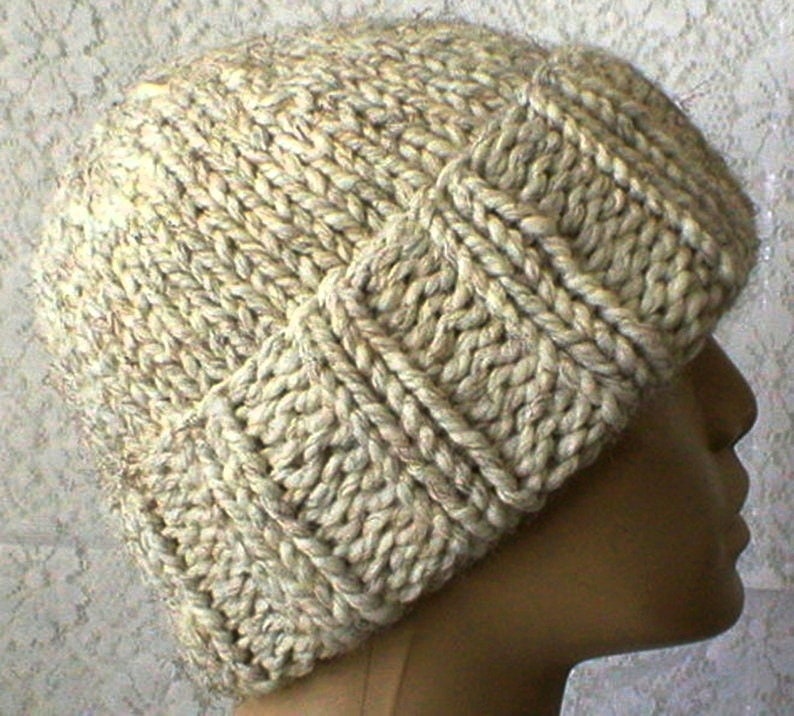 May include: A beige knitted hat with a textured pattern. The hat is made from thick yarn and has a slouchy fit.