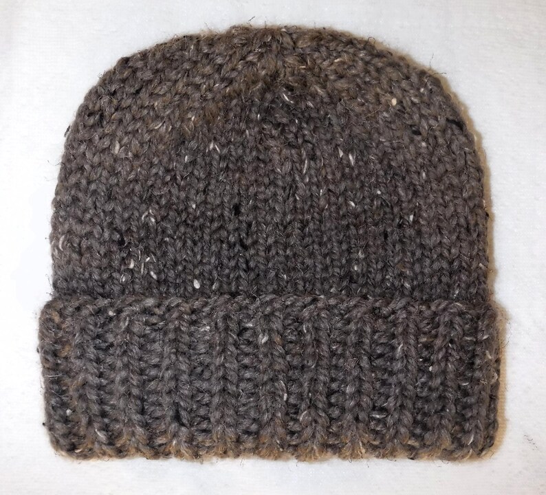 May include: A dark grey knitted beanie hat with a folded-up brim. The hat is made from a thick, textured yarn with white flecks. A classic winter accessory, perfect for keeping warm.