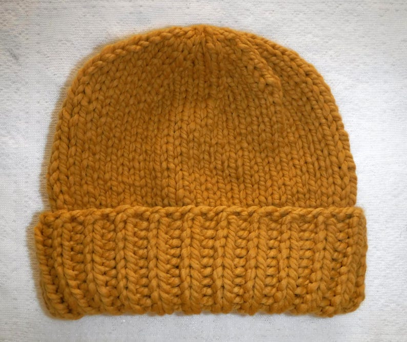 May include: Mustard yellow knit beanie hat. The hat is made of thick yarn and features a ribbed brim. The top portion of the hat has a simple knit pattern. This warm hat is perfect for cold weather.