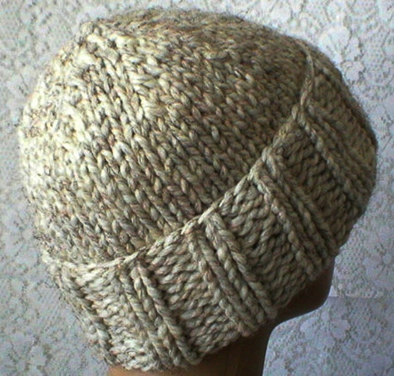 May include: A beige knitted hat with a unique stitch pattern. The hat has a slouchy fit and is made with a soft, textured yarn.