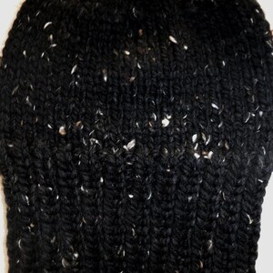 Puede incluir: Primer plano de un gorro negro tejido con motas blancas. El gorro est&aacute; hecho de un hilo grueso y texturizado, y el patr&oacute;n de tejido es visible. El gorro parece c&aacute;lido y acogedor.