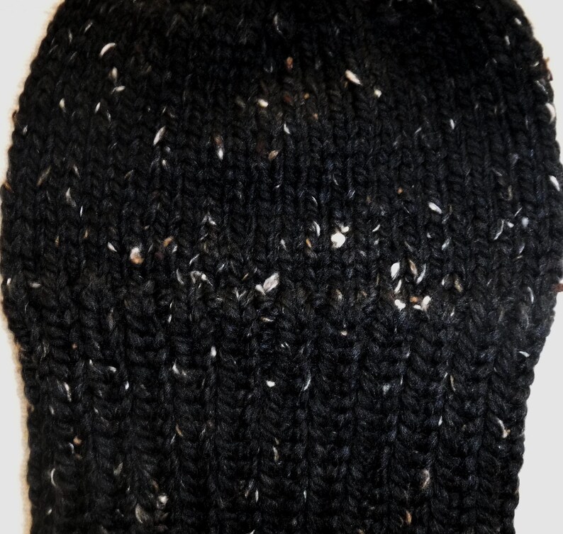 Puede incluir: Primer plano de un gorro negro tejido con motas blancas. El gorro est&aacute; hecho de un hilo grueso y texturizado, y el patr&oacute;n de tejido es visible. El gorro parece c&aacute;lido y acogedor.