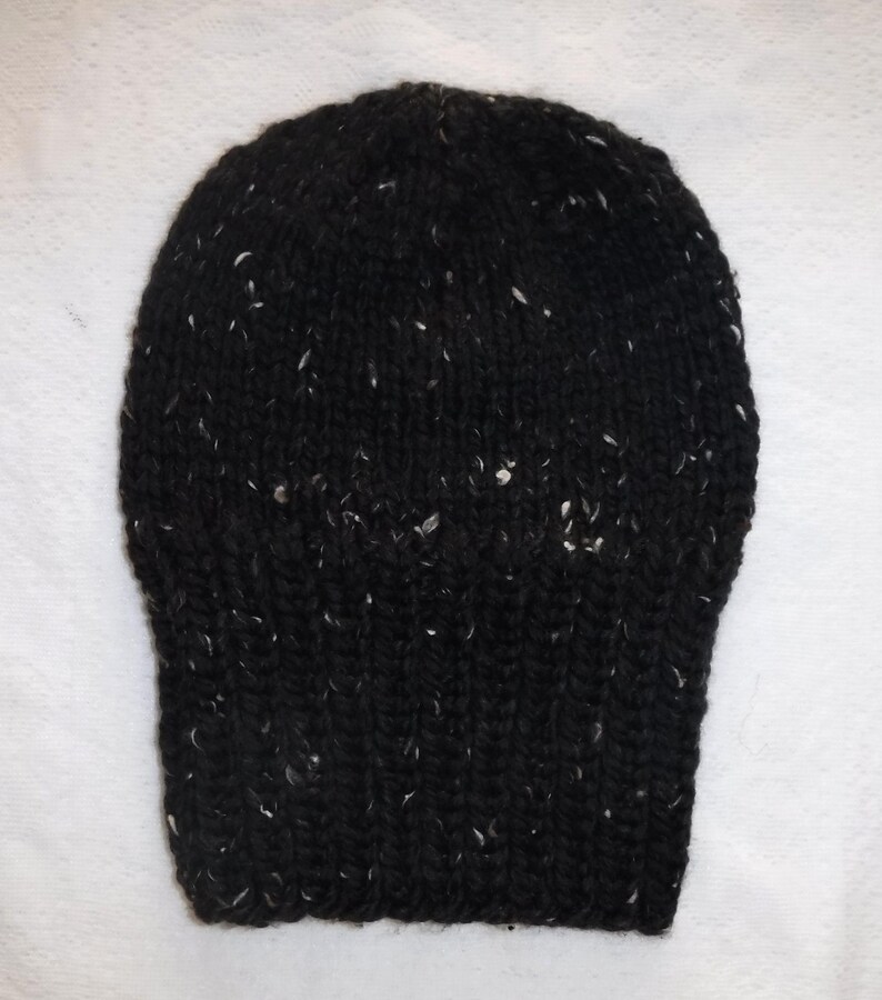 Puede incluir: Un gorro negro tejido con motas blancas. El gorro tiene un borde acanalado y una parte superior redondeada. El hilo parece ser un material grueso y c&aacute;lido, adecuado para el clima fr&iacute;o.