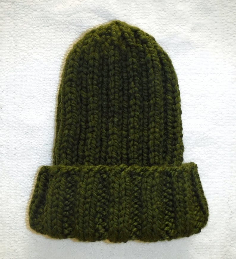 Op de afbeelding: Een donker olijfgroene gebreide muts met een omgeslagen rand. De muts is gemaakt van dik garen en heeft een geribbelde textuur. Een winteraccessoire.