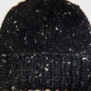 Puede incluir: Un gorro negro tejido con motas blancas. El gorro tiene un borde acanalado y una textura de tejido apretado. Este c&aacute;lido gorro de invierno es ideal para el fr&iacute;o.