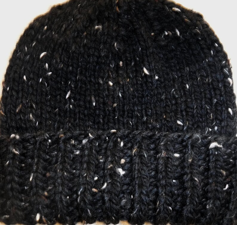 Puede incluir: Un gorro negro tejido con motas blancas. El gorro tiene un borde acanalado y una textura de tejido apretado. Este c&aacute;lido gorro de invierno es ideal para el fr&iacute;o.