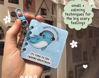 May include: A small, light blue notebook with a cartoon whale wearing headphones. The notebook has a blue clip and the text "ITS TIME TO TRY SQUARE BREATHING". The image also includes the text "small + calming techniques for the big scary feelings".