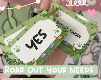 May include: A set of green communication cards held together by a green plastic ring. Each card features a white center with black text, including the word YES, surrounded by a border decorated with small cartoon dinosaurs, trees, and stars.