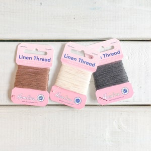 May include: Three spools of 100% linen thread in brown, white, and grey. Each spool is labelled "Linen Thread Premium Quality" and "Hemline".