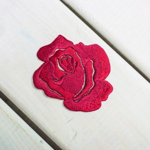 May include: A red embroidered rose patch. The rose is detailed with multiple layers of petals.