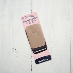 May include: A pack of 10 iron-on patches in a variety of colours, including white, grey, navy, black, brown and beige. The pack is pink with the text "Iron-On Patches" and "Hemline" printed on it.