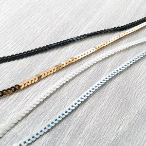 May include: Four strands of sequined trim in black, gold, white and light blue.