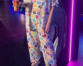 May include: A person in a colourful pajama set featuring a repeating pattern of shapes and colours. The set includes a short-sleeved shirt, a crop top, and matching trousers. The person is holding a can with a vibrant label.