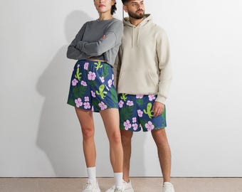 May include: A woman and a man in matching blue shorts with a floral and cactus design. The woman wears a grey long-sleeved top, and the man wears a beige hoodie. Both are wearing white trainers.