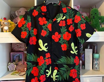 May include: Black button-down shirt with a vibrant floral pattern. The shirt features large red hibiscus flowers, green banana-shaped figures, and green palm leaves. The shirt is hanging on a white hanger.