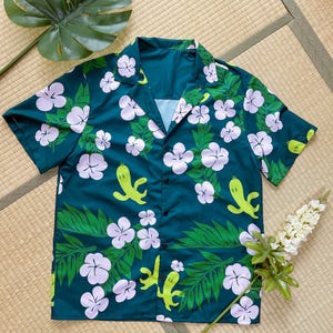 May include: A teal blue short-sleeved button-up shirt with a tropical print featuring green leaves, white flowers, and yellow cartoon characters.