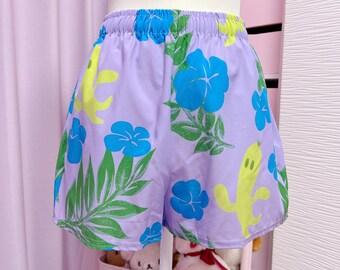 May include: Lilac shorts with an elasticated waistband, decorated with a bright floral pattern. The design includes blue hibiscus flowers, green leaves, and yellow cactus shapes. These shorts offer a comfortable and colourful style.