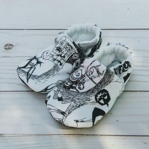 May include: A pair of white baby booties with black and white illustrations of characters from the movie The Nightmare Before Christmas. The booties have a soft, comfortable fabric and are perfect for keeping little feet warm.