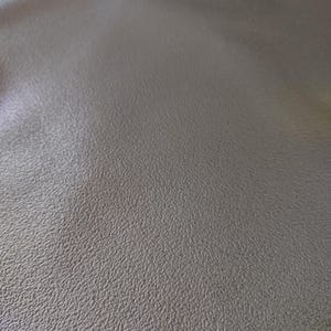 May include: Close-up of a gray textured fabric with a subtle sheen. The fabric has a fine, even grain and a smooth, slightly pebbled surface.