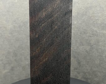 May include: A rectangular block of dark brown wood with a visible grain pattern. The wood has a rich, natural colour and texture. The block is standing upright against a neutral background.
