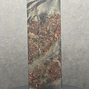 Op de afbeelding: Een rechthoekig houten blok met een uniek, natuurlijk nerfpatroon. Het hout heeft een mix van donkerbruine, roodbruine en grijze tinten, wat een visueel interessante textuur creëert. Het blok staat rechtop en toont zijn gedetailleerde oppervlak.