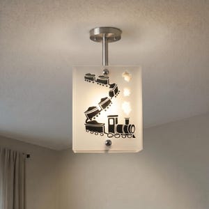 May include: A rectangular ceiling light fixture with a frosted glass shade featuring a black graphic of a steam locomotive pulling coal cars. The fixture is mounted to the ceiling with a brushed metal stem and circular base, emitting a warm glow.