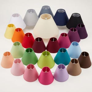 May include: A selection of colourful lampshades in a variety of shades, such as white, grey, yellow, orange, red, green, teal, blue, brown, pink, purple, and black. The lampshades are arranged in a circular pattern, displaying their diverse colours and conical shapes.