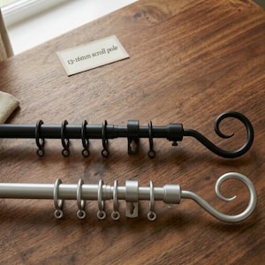May include: Two scroll-style curtain poles, one black and one silver, are displayed on a wooden surface. Each pole features rings for hanging curtains and a decorative curled end. A small card reads "13-16mm scroll pole."