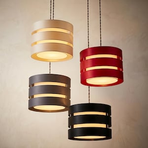 May include: Four contemporary pendant lights in cream, red, grey, and black. Each cylindrical shade has horizontal cutouts that emit light. The lights hang from dark cords, offering a modern lighting solution.