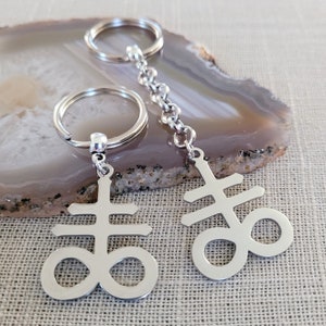 May include: Two silver keychains with a silver chain connecting them. Each keychain has a silver charm in the shape of a pentagram with a circle around it.