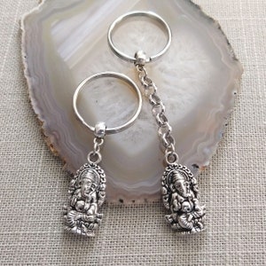 May include: Two silver keychains with a detailed Ganesha charm on each. The keychains are connected by a silver chain.