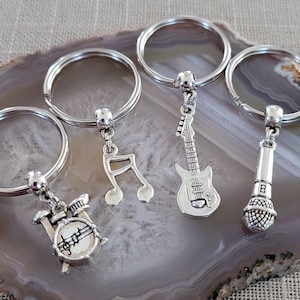 May include: Four silver keychains with different music-themed charms: a guitar, a microphone, a music note, and a drum set.