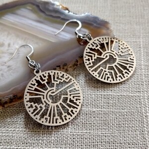 May include: A pair of silver earrings with a circular design featuring a tree of life pattern.